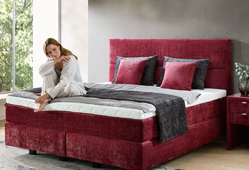 rotes Boxspringbett mit Model, die gemütlich darauf sitzt