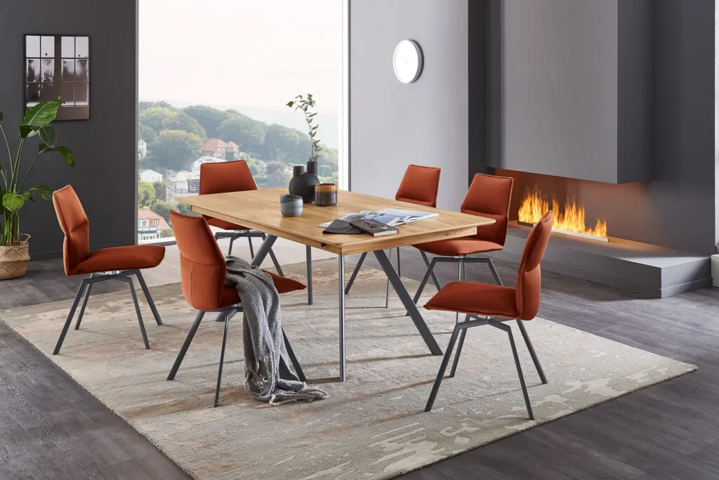 Esszimmer mit ausgefallennen Esszimmerstühlen einen Holz design Tisch. Kaminfeuer in der Wand. Schöner ausblick aus dem Großen Fenster