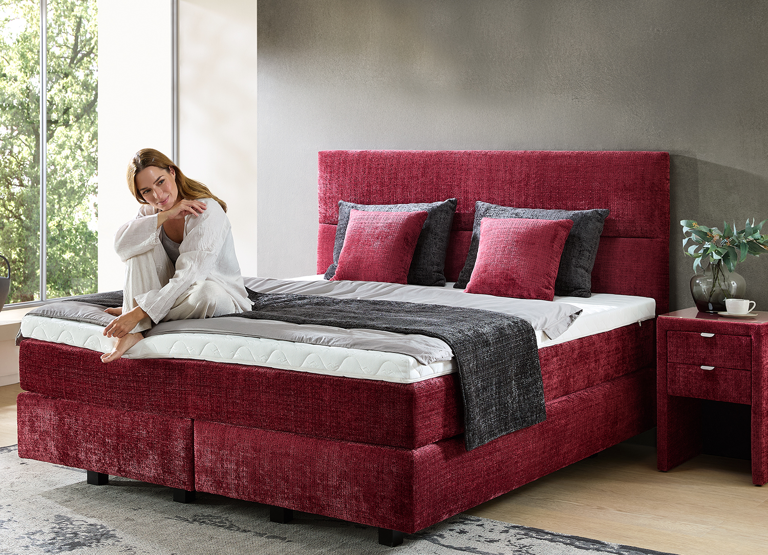 Boxspringbett in rot mit einer Dame die auf dem Bett hockt und lächelt