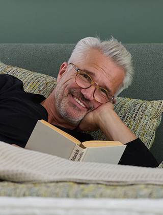 Mann liegt lächelnd mit einem Buch im Bett